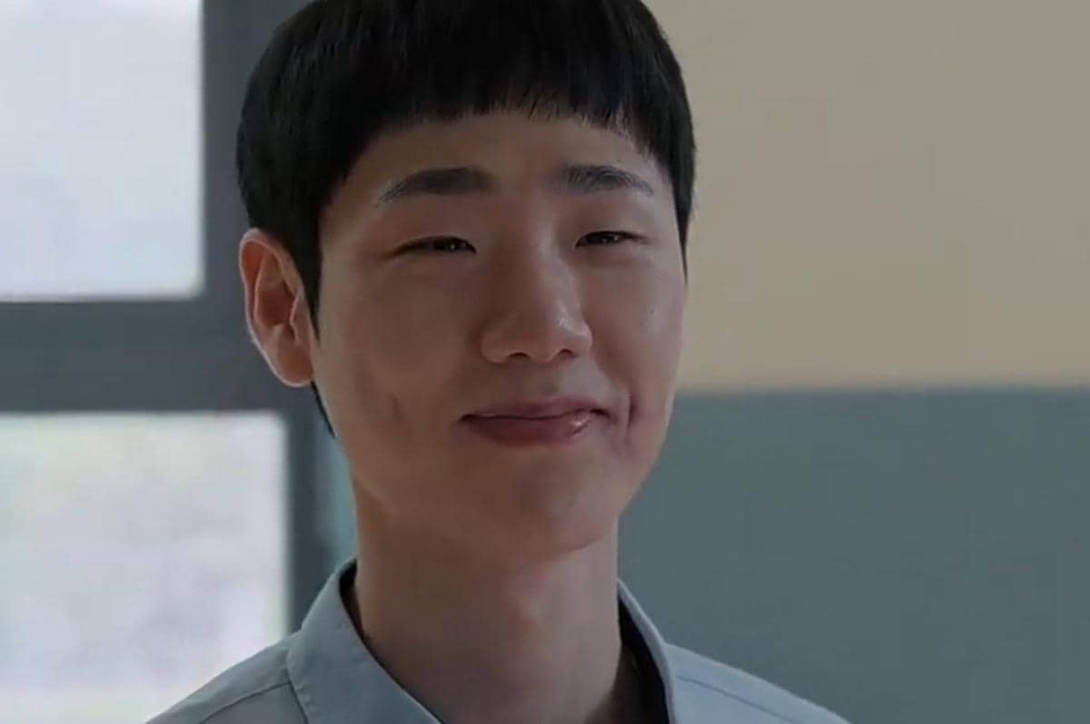 Seorang pria muda tersenyum lembut di dalam ruangan dengan latar belakang jendela, diambil dari serial Netflix Teach You a Lesson.
