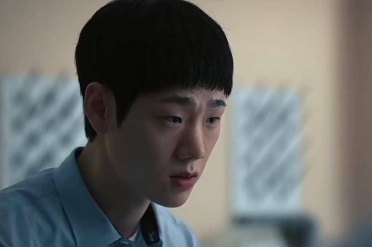 Seorang pria muda mengenakan kemeja biru tampak serius menatap ke depan dalam adegan serial Teach You a Lesson di Netflix.