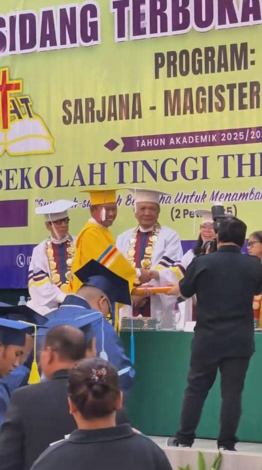 Seorang wisudawan lanjut usia mengenakan toga kuning menerima ijazah dari pejabat kampus dalam acara wisuda di sebuah sekolah tinggi teologi.