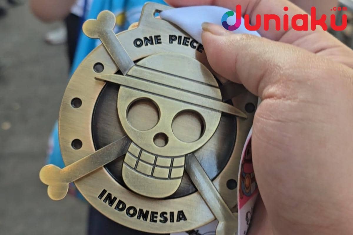 Seseorang memegang medali ONE PIECE Run 2026 berwarna emas dengan logo tengkorak khas dan tulisan Indonesia di bagian bawah.