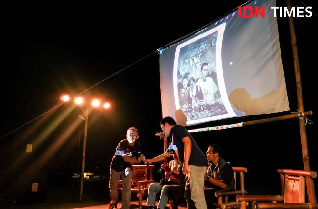 Beberapa peserta berdiskusi di depan layar proyektor besar pada malam hari dalam tahap produksi Gunungan Film.