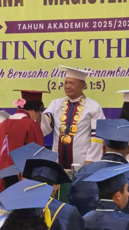 Seorang wisudawan lanjut usia mengenakan toga merah menerima ucapan selamat dari rektor berpakaian toga putih di acara wisuda perguruan tinggi.