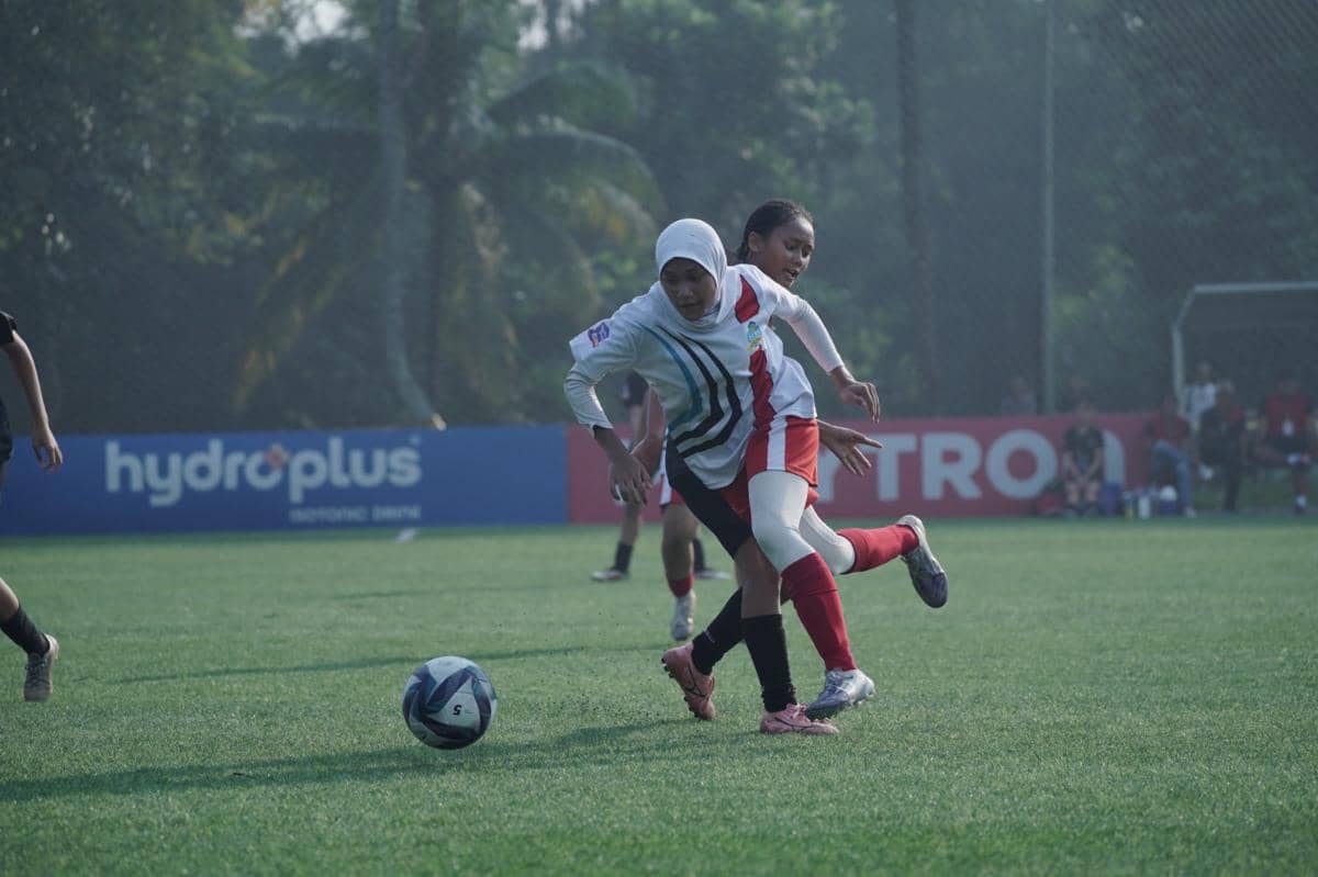 Dua pemain sepak bola perempuan berebut bola di lapangan hijau dalam ajang Hydroplus Soccer League Jakarta.