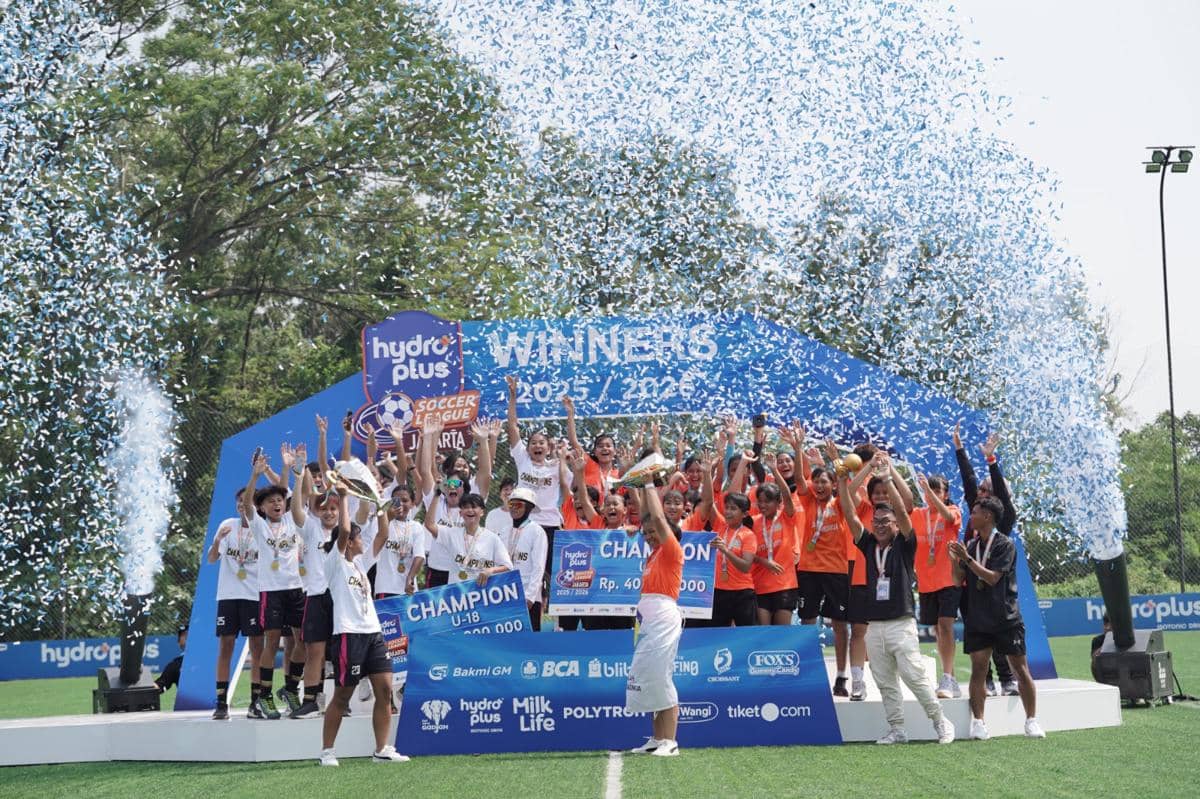 Para pemain muda merayakan kemenangan di panggung juara Hydroplus Soccer League Jakarta 2023/2024 dengan konfeti biru di udara.
