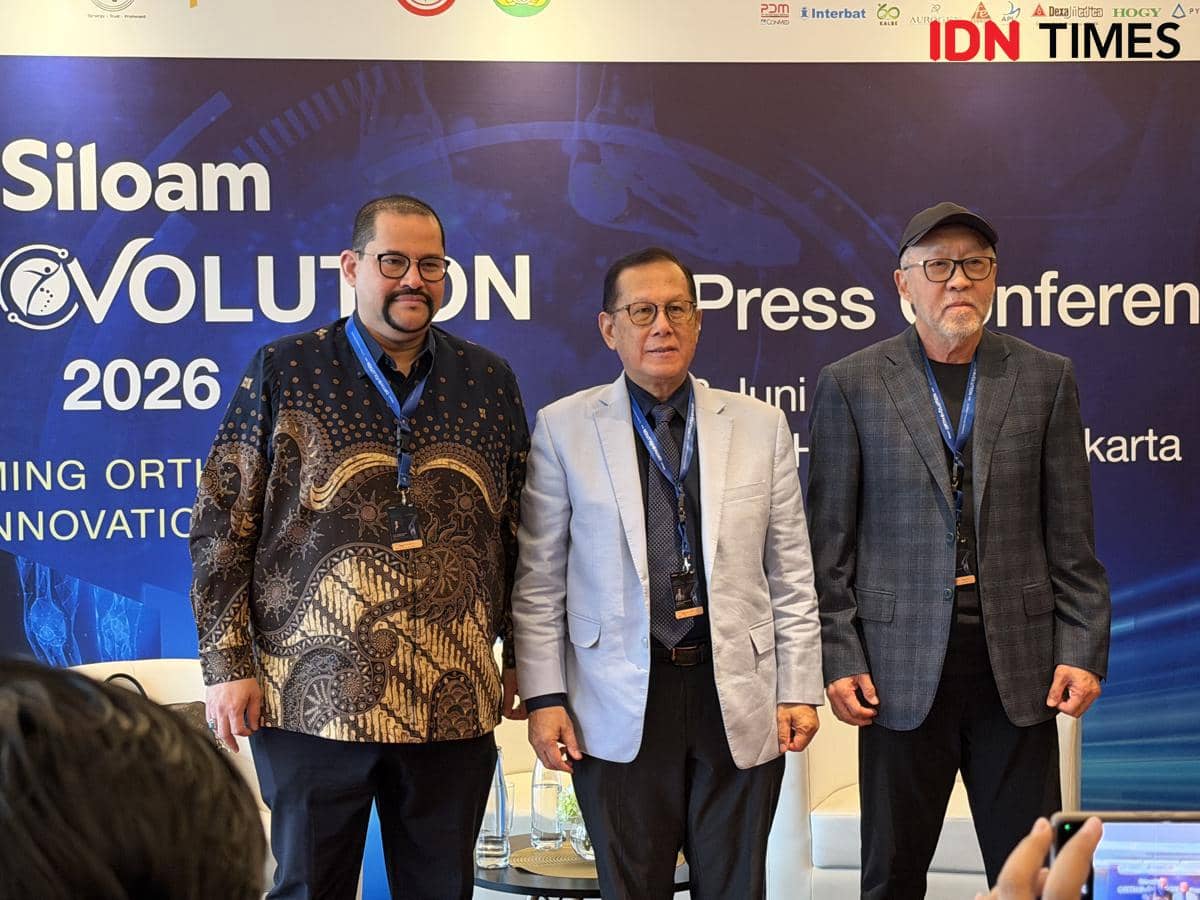Tiga pria berpose di depan latar bertuliskan Siloam Orthovolution 2026 saat konferensi pers di Jakarta, mengenakan pakaian formal dan kartu identitas.