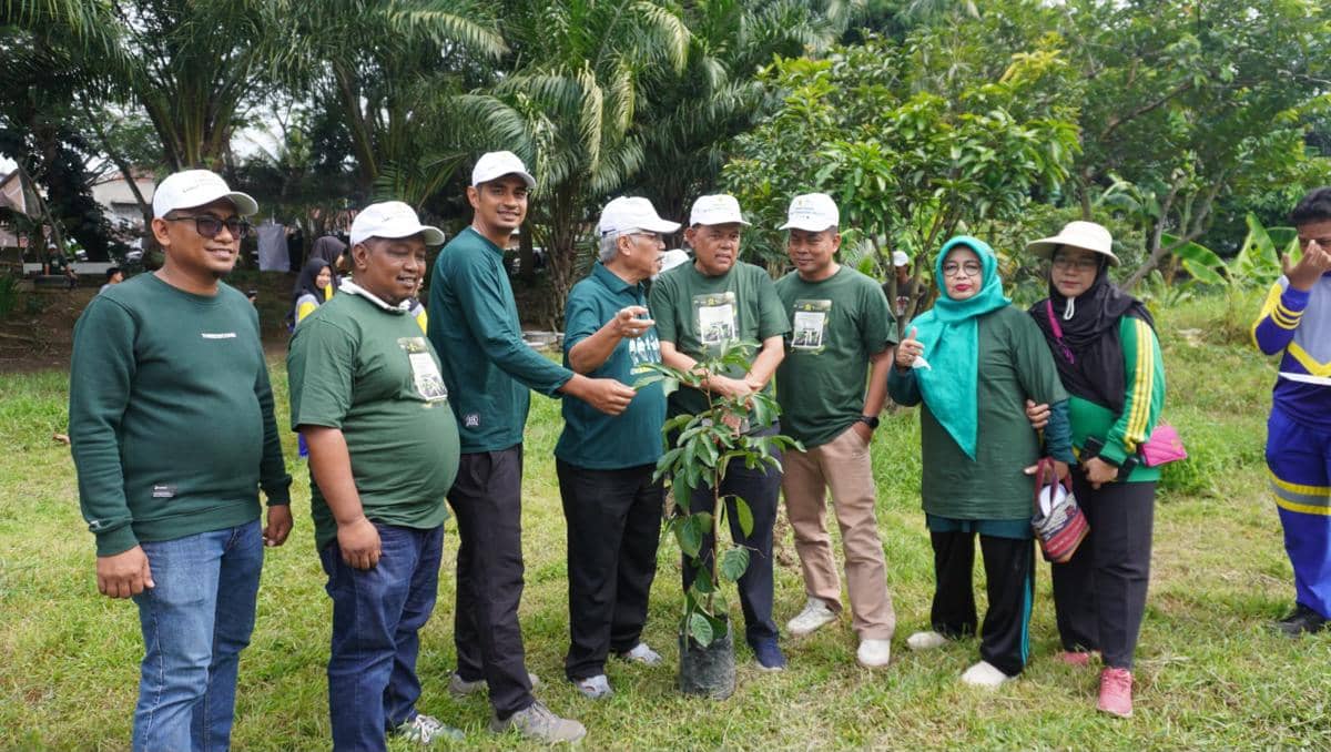 Sekelompok orang mengenakan pakaian hijau dan topi putih berpose bersama bibit pohon di tepi Sungai Deli dalam kegiatan penanaman pohon.