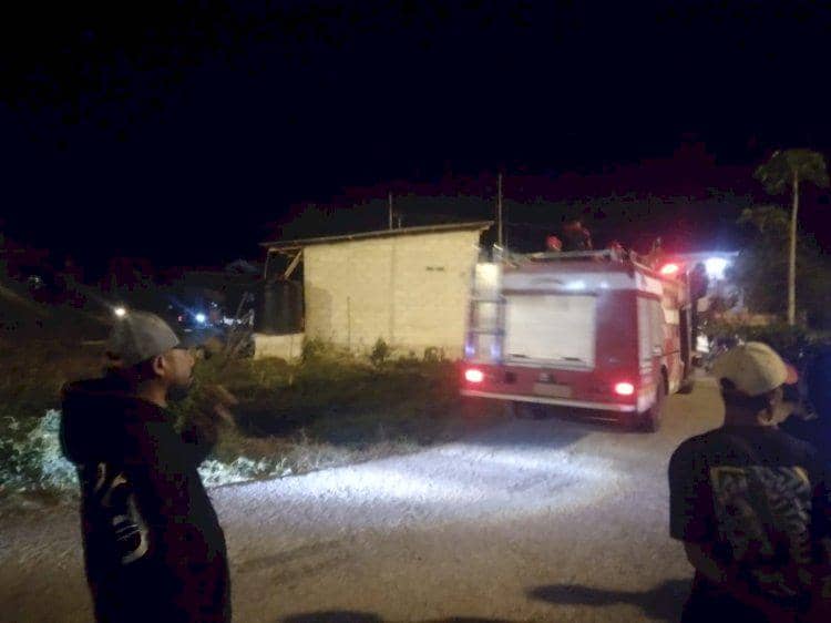 Mobil pemadam kebakaran berada di depan rumah yang terbakar pada malam hari di Kupang, disaksikan beberapa warga di lokasi.