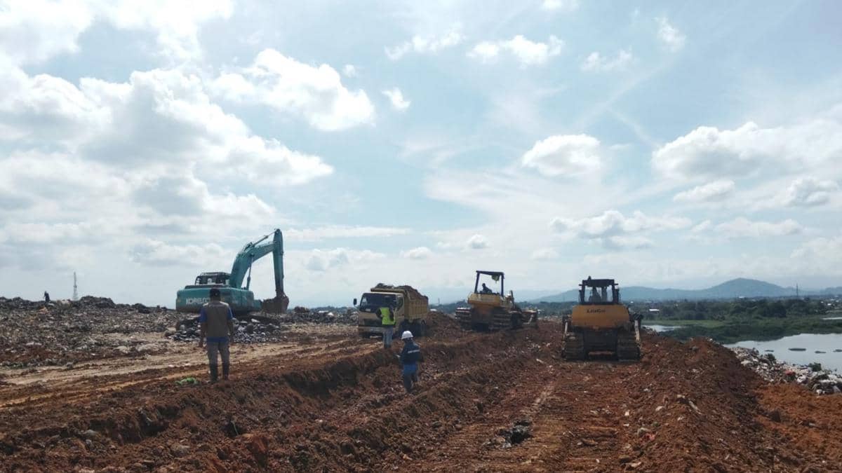 Alat berat dan pekerja melakukan pembenahan TPA Antang di Makassar dengan metode cover soil di bawah langit cerah.