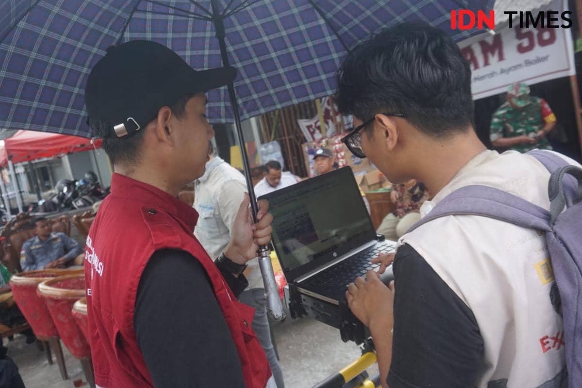 Dua anggota tim geofisika UGM memeriksa data georadar di laptop sambil berteduh di bawah payung saat penyelidikan di Sleman.