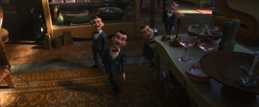Empat boneka ventriloquis berjas hitam dengan dasi kupu-kupu merah berjalan di dalam ruangan antik penuh perabot dan piring kaca.