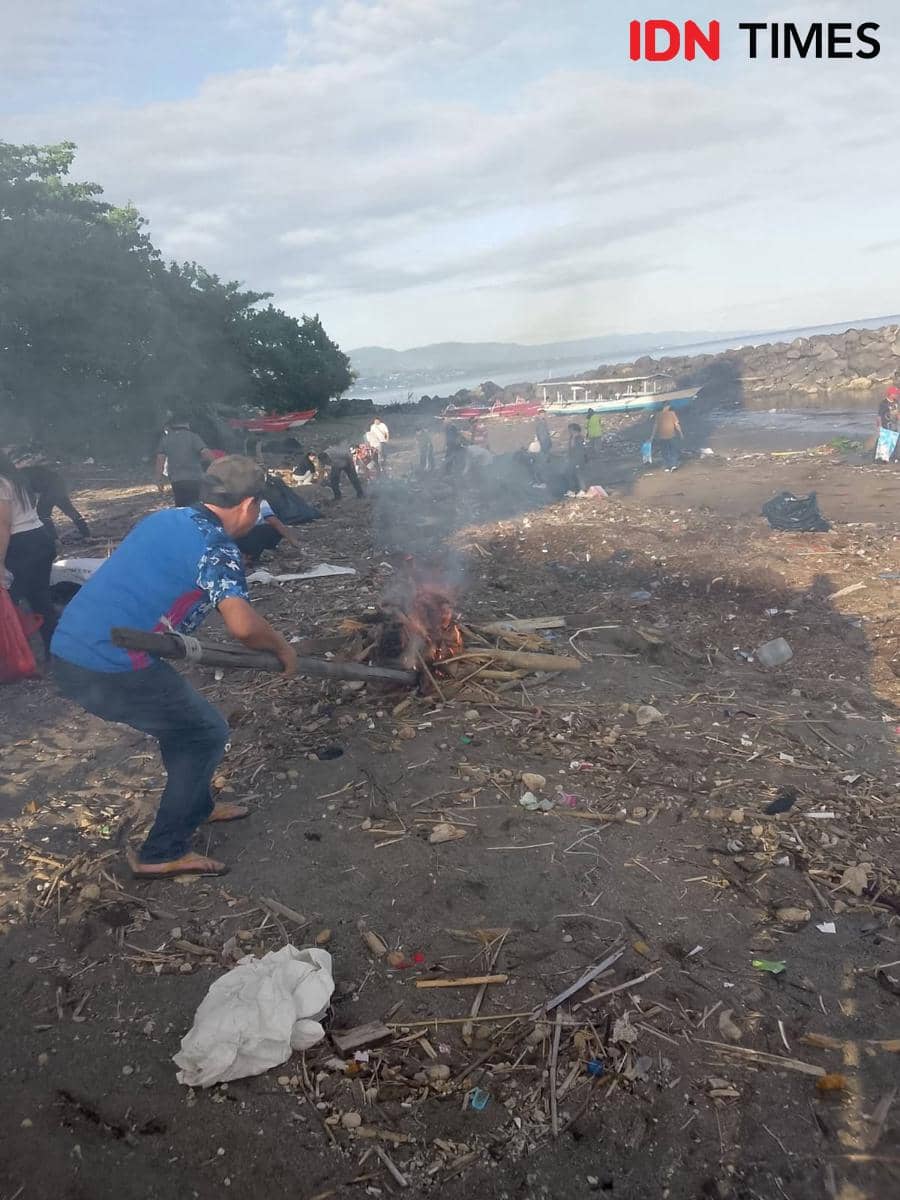 Sejumlah warga beraktivitas di pesisir pantai Manado, Sulawesi Utara, dengan latar api unggun kecil dan perahu di tepi laut.