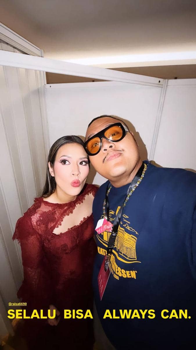 Seorang wanita mengenakan gaun merah berpose bersama pria berkacamata hitam oranye saat menghadiri konser Raisa Love & Let Go 2026.