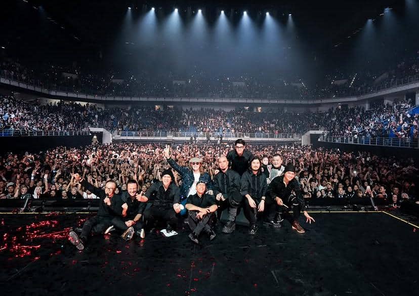 Para personel band berpose di atas panggung besar dengan latar penonton yang memenuhi arena konser di Kuala Lumpur.