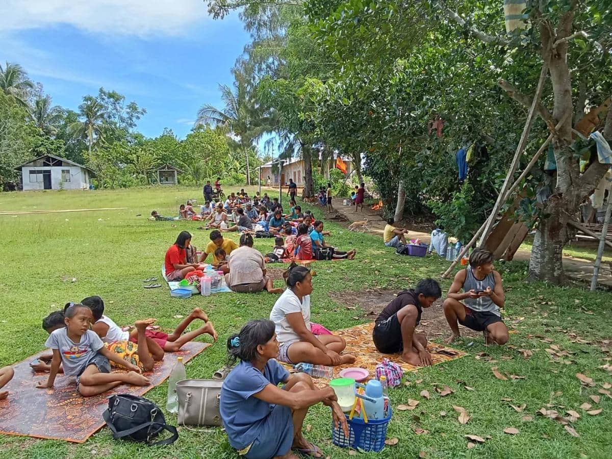 Sejumlah warga duduk di atas tikar di area terbuka berlatar pepohonan dan rumah sederhana setelah gempa di Kepulauan Sangihe.