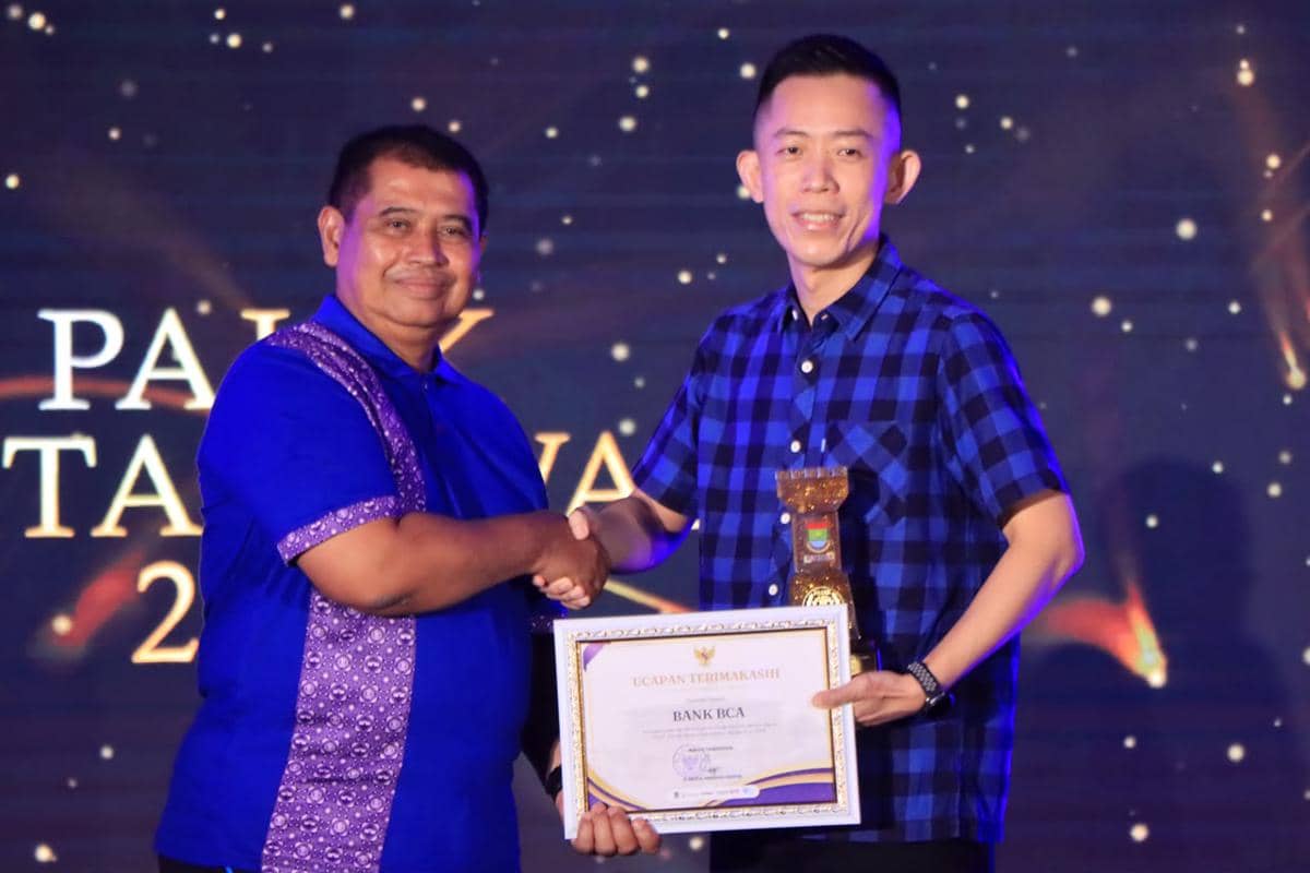 Dua pria berjabat tangan di atas panggung, salah satunya memegang piagam penghargaan dan trofi dalam acara apresiasi pajak di Tangerang.