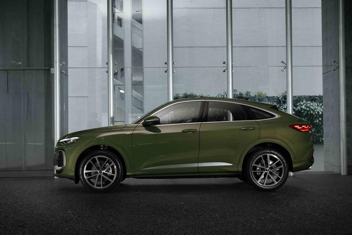 Mobil SUV berwarna hijau metalik diparkir di area gedung modern dengan dinding kaca besar dan pencahayaan alami.