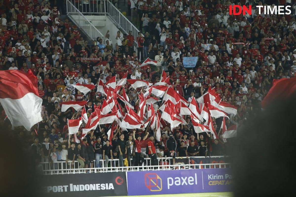 Suporter timnas Indonesia U-19 mengenakan pakaian merah dan putih sambil mengibarkan bendera merah putih di tribun Stadion Utama Sumatra Utara.