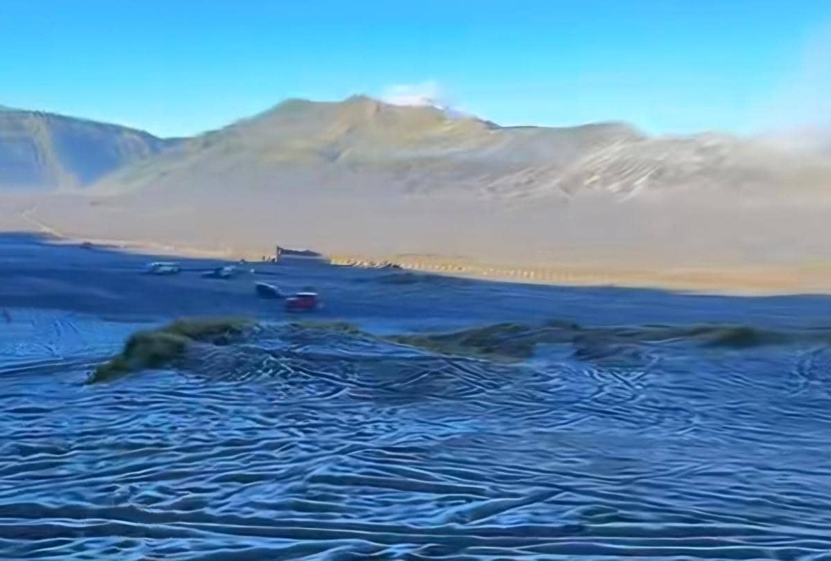 Pemandangan embun upas yang membeku di kawasan Gunung Bromo dengan latar pegunungan dan langit biru cerah di pagi hari.