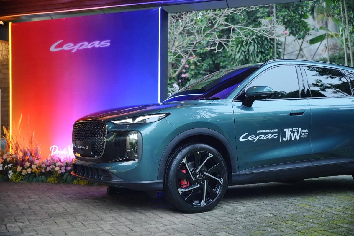 Mobil Lepas LS berwarna hijau metalik dipamerkan di acara Jakarta Fashion Week 2027 dengan latar pencahayaan gradasi biru dan merah.