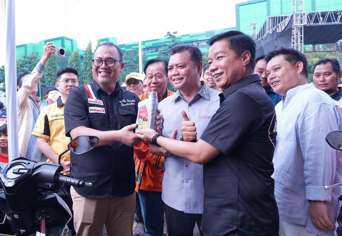 Beberapa pria tersenyum sambil memegang botol pelumas motor dalam acara kolaborasi Pertamina dan Hasston di area luar ruangan.