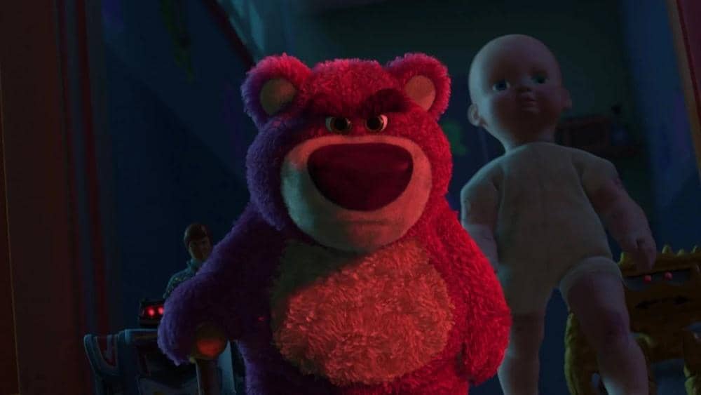 Boneka beruang berwarna ungu dengan ekspresi marah berdiri di depan, diikuti boneka bayi di latar belakang dalam adegan film animasi.