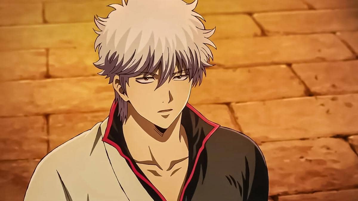 Karakter anime berambut perak mengenakan kimono hitam dan putih dengan latar jalan berbatu berwarna oranye hangat.