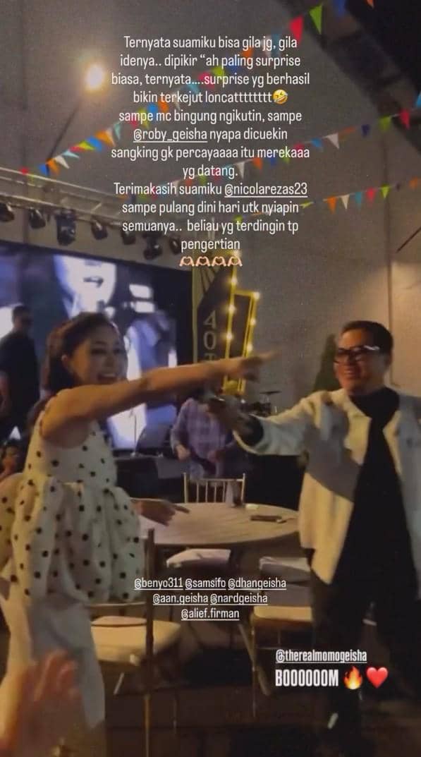 Momo mengenakan gaun putih bermotif polkadot sedang bernyanyi dan tersenyum bersama anggota band Geisha di sebuah acara panggung malam hari.