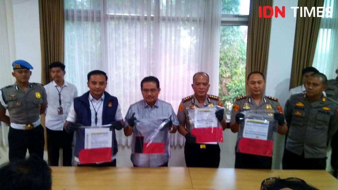 Beberapa petugas kepolisian dan penyidik berdiri di depan meja sambil memegang barang bukti dalam kantong plastik terkait kasus penipuan skema ponzi.