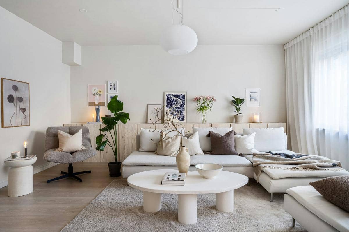 Ruang tamu bernuansa putih dengan sofa modern, meja bundar, tanaman hias, dan dekorasi dinding minimalis bergaya Skandinavia.