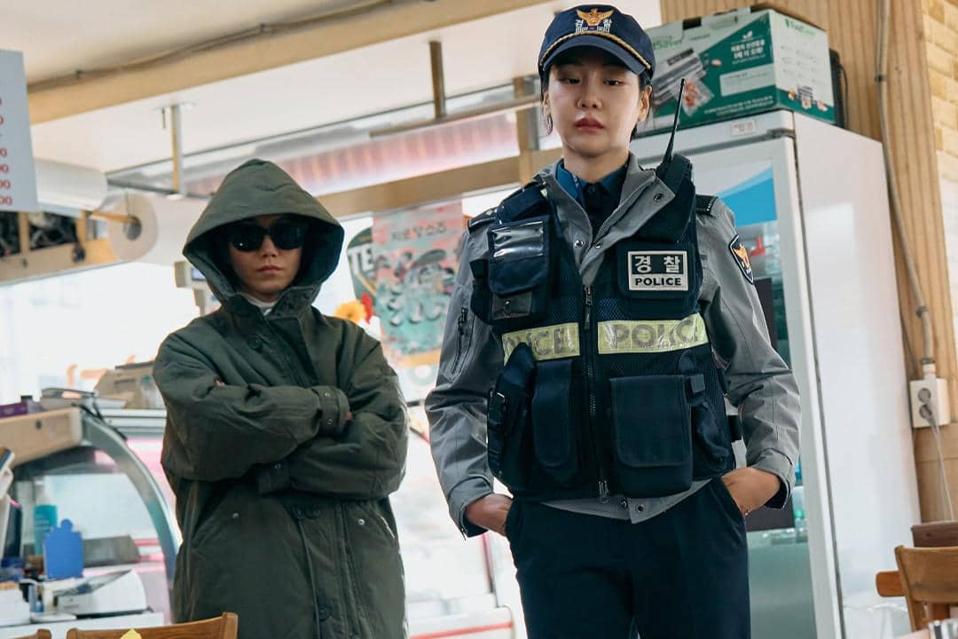 Dua karakter dalam drama Fifties Professionals, satu mengenakan seragam polisi dan satu lagi memakai jaket tebal dengan tudung dan kacamata hitam.