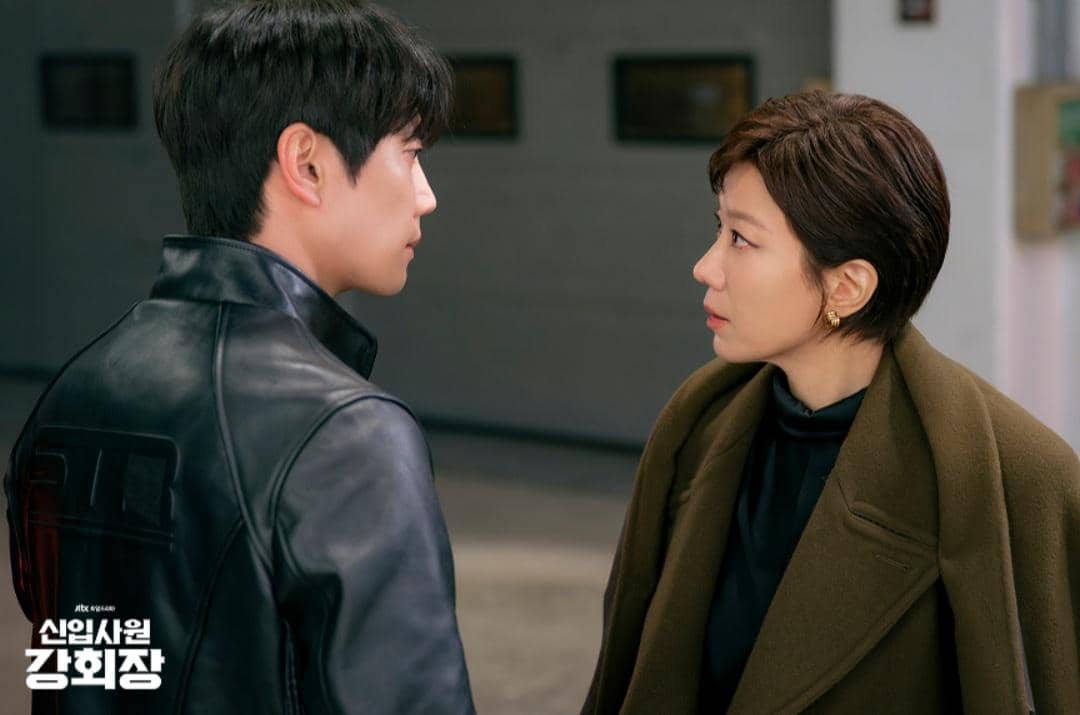 Dua karakter dalam drama Korea Reborn Rookie saling menatap serius di sebuah ruangan, mengenakan jaket kulit dan mantel cokelat.