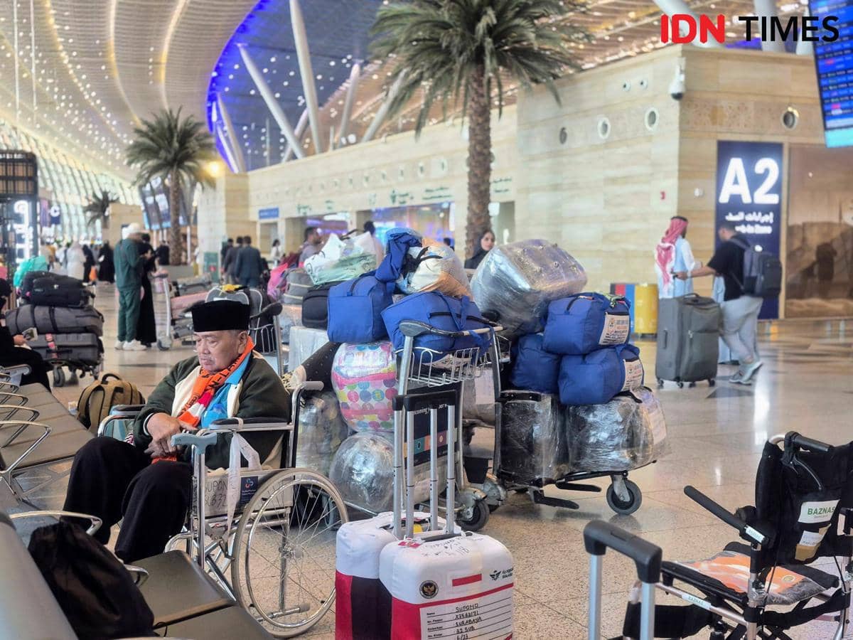 Seorang jemaah haji duduk di kursi roda di Terminal Internasional King Abdulaziz Jeddah dengan tumpukan bagasi di sekitarnya.