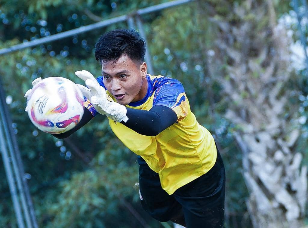 Seorang penjaga gawang Arema FC mengenakan jersey kuning dan sarung tangan putih sedang menangkap bola di lapangan latihan.