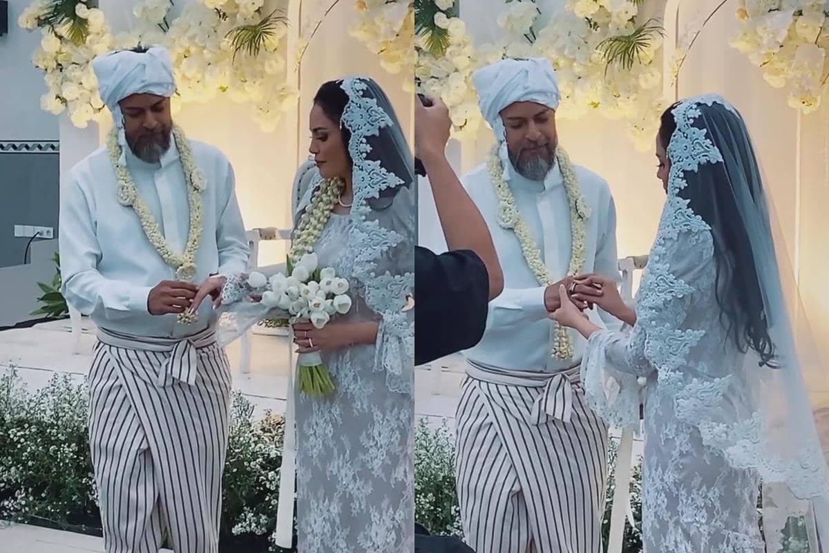 Pasangan pengantin mengenakan busana adat berwarna putih saling bertukar cincin di pelaminan berhias bunga putih.