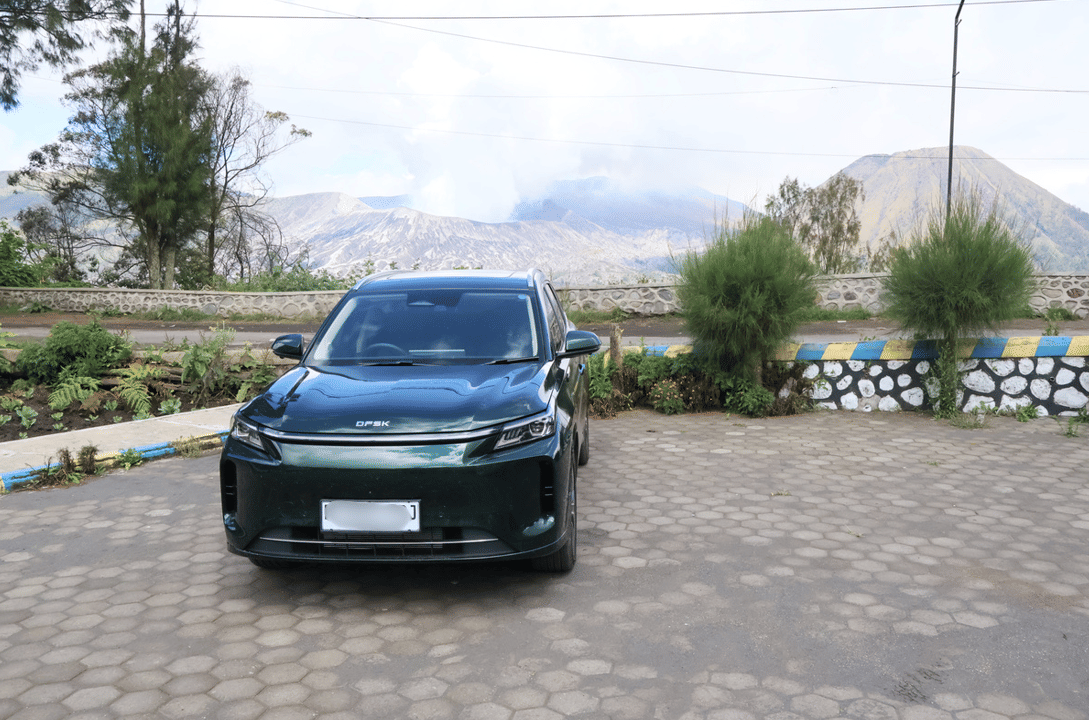 Mobil SUV berwarna hijau tua dengan desain modern dan mewah terparkir di area pegunungan dengan latar pemandangan alam.