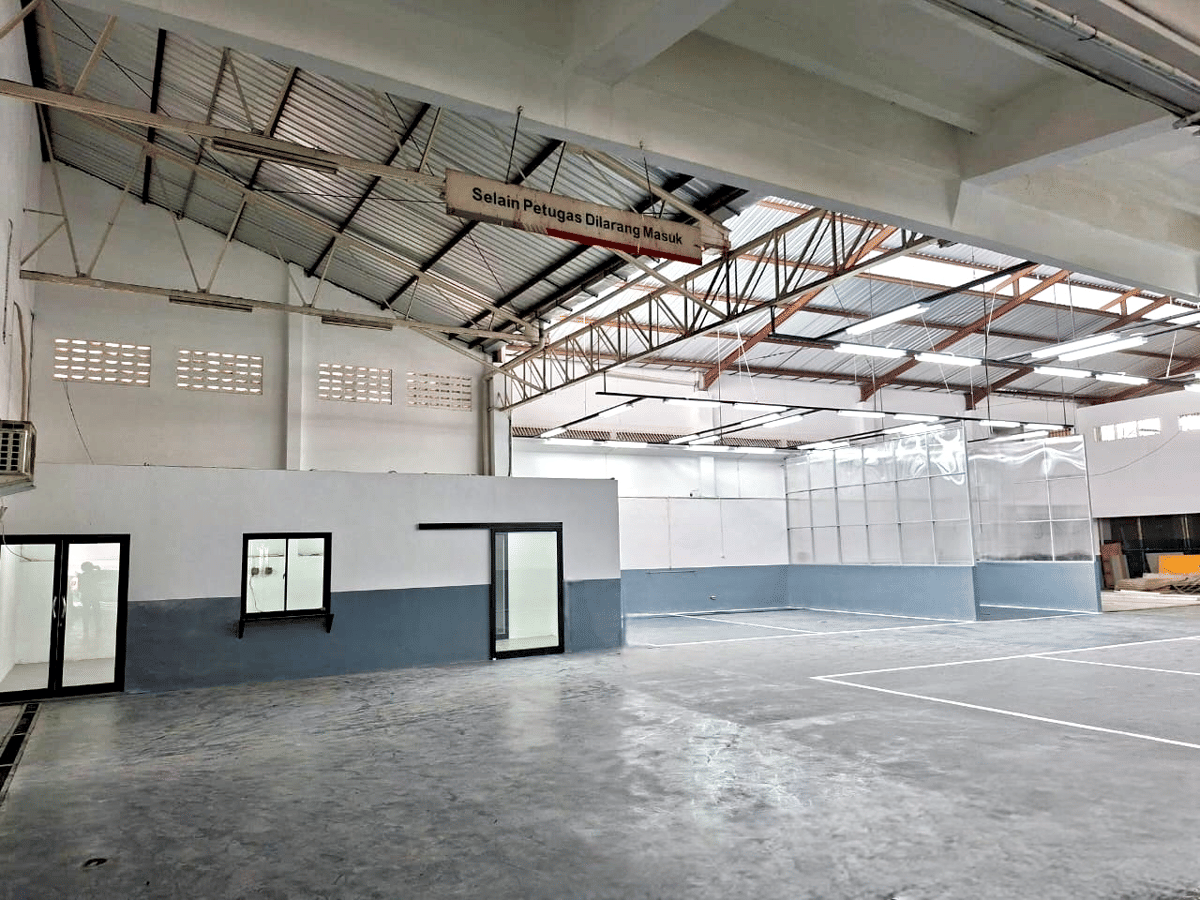 Area service bay luas dengan lantai beton, dinding berwarna abu-abu dan putih, serta atap baja ringan dengan pencahayaan lampu neon.