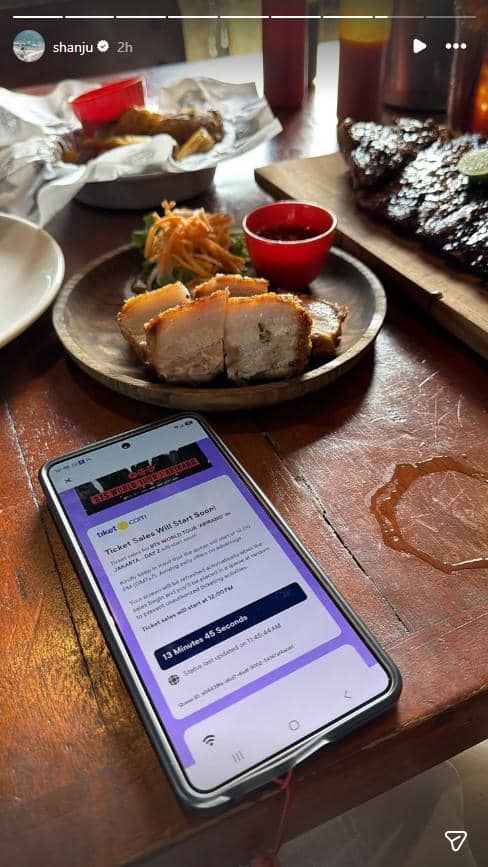 Ponsel menampilkan situs penjualan tiket konser BTS di atas meja kayu dengan hidangan daging panggang dan makanan pendamping.