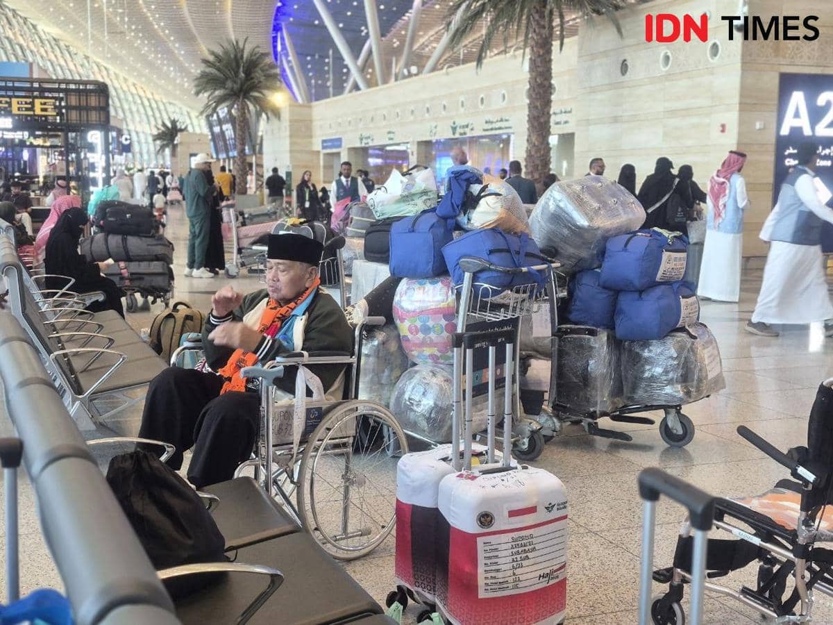 Seorang jemaah haji Indonesia duduk di kursi roda di Terminal Internasional Bandara King Abdulaziz Jeddah dengan tumpukan bagasi di sekitarnya.