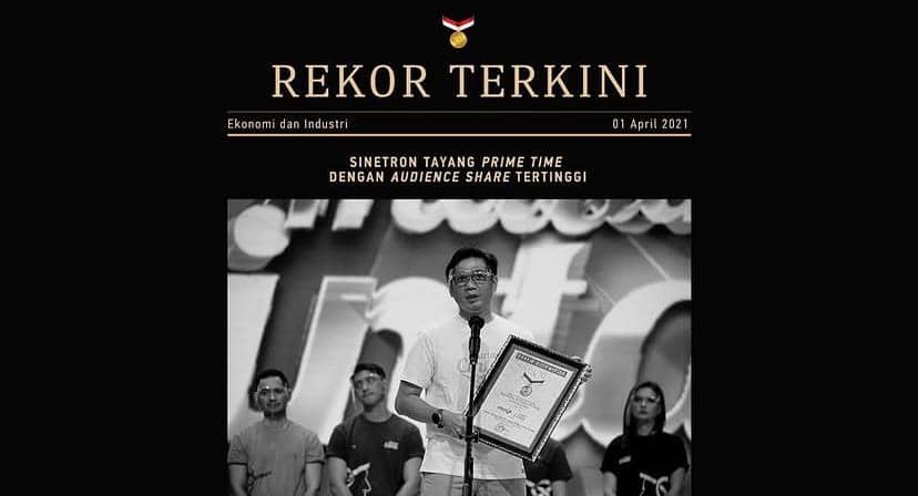 Seorang pria memegang piagam penghargaan MURI di atas panggung bersama beberapa orang lain, dengan latar bertuliskan rekor terkini.