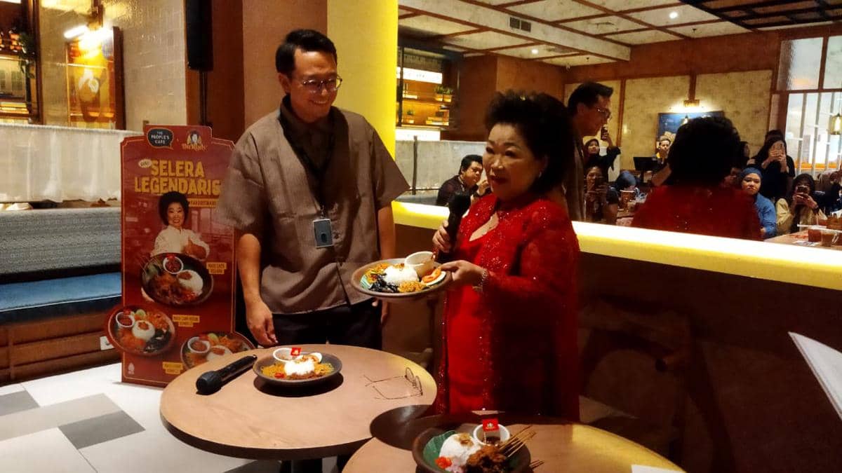 Seorang wanita mengenakan kebaya merah memperkenalkan menu kolaborasi kuliner dengan seorang pria di restoran, menampilkan hidangan nasi dan sambal khas.