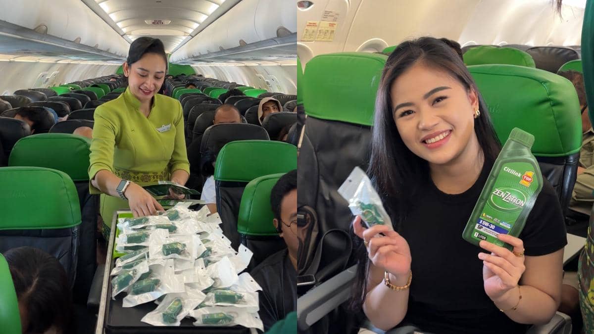 Pramugari membagikan paket hadiah kepada penumpang di dalam kabin pesawat dengan kursi hijau, sementara seorang penumpang tersenyum sambil memegang botol oli dan suvenir.