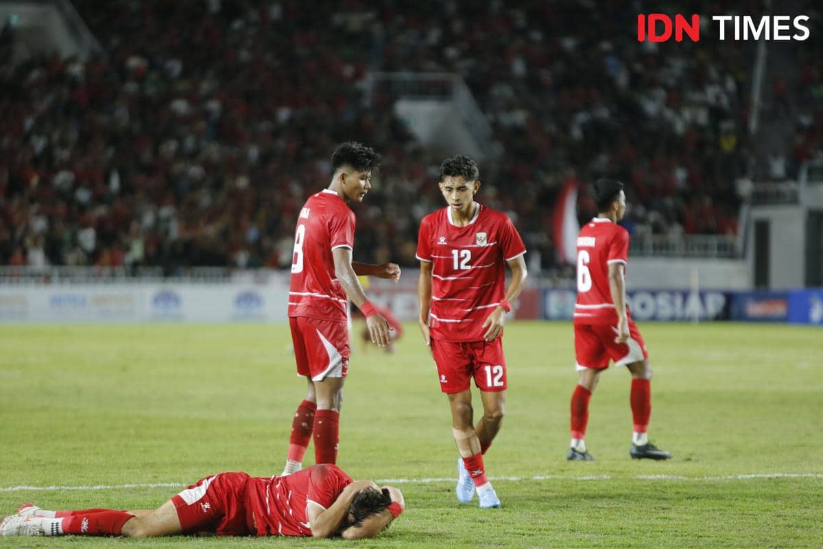 Pemain Timnas Indonesia U-19 mengenakan seragam merah di lapangan Stadion Utama Sumut, salah satu pemain tampak terbaring di rumput.