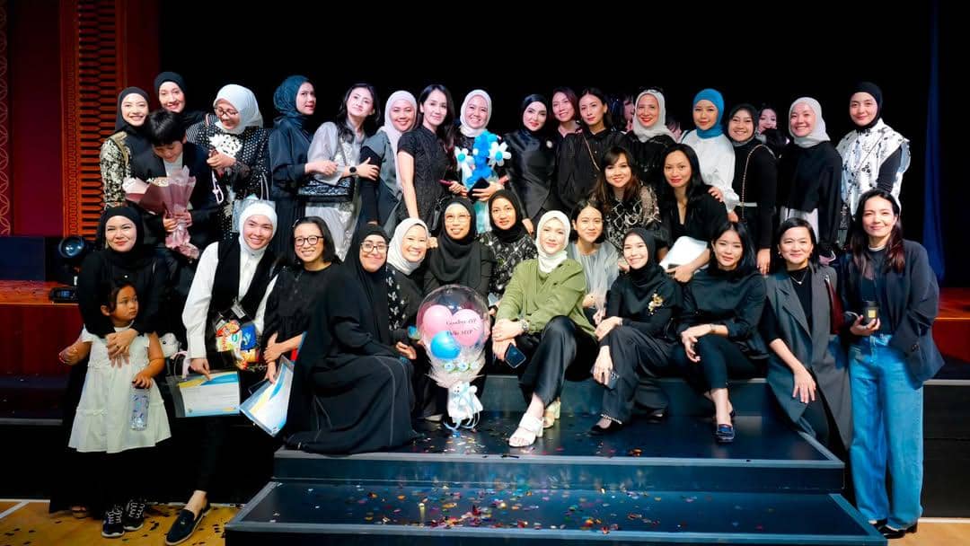 Sekelompok wanita berpose bersama di atas panggung setelah acara kelulusan sekolah dasar, sebagian mengenakan busana hitam dan hijab.