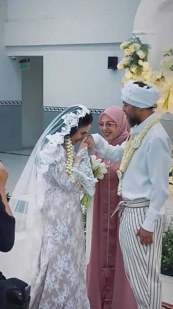 Pasangan pengantin mengenakan busana adat Sunda berwarna putih dan abu-abu saat prosesi pernikahan di depan dekorasi bunga kuning.