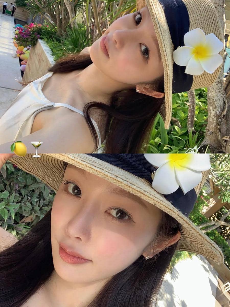 Seorang perempuan mengenakan topi jerami berhias bunga kamboja putih berpose di area outdoor dengan latar pepohonan dan kolam di Bali.