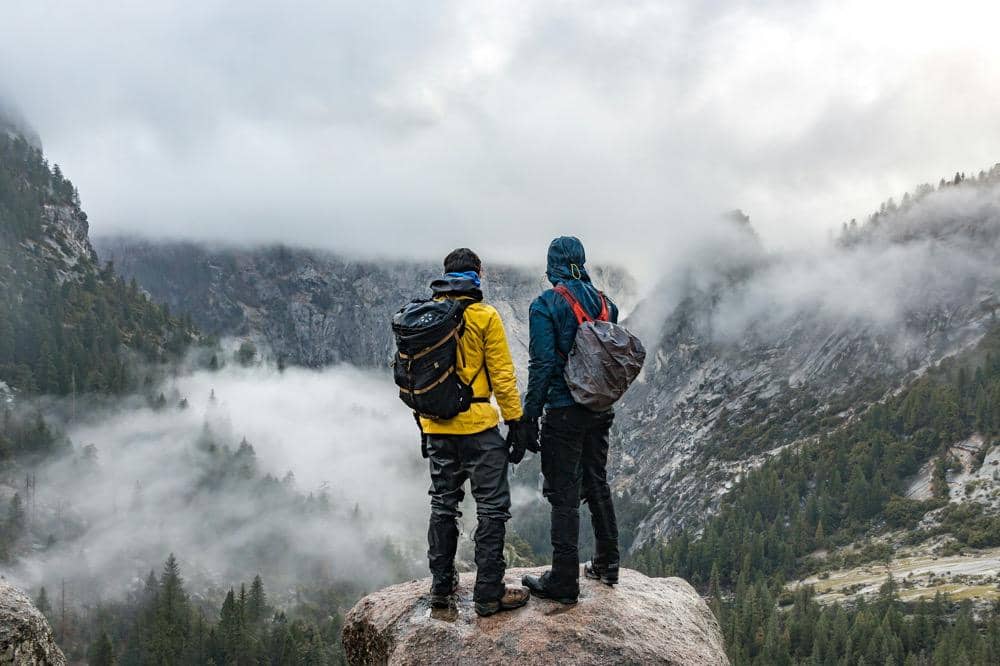 Dua pendaki berdiri di atas tebing dengan jaket gunung
