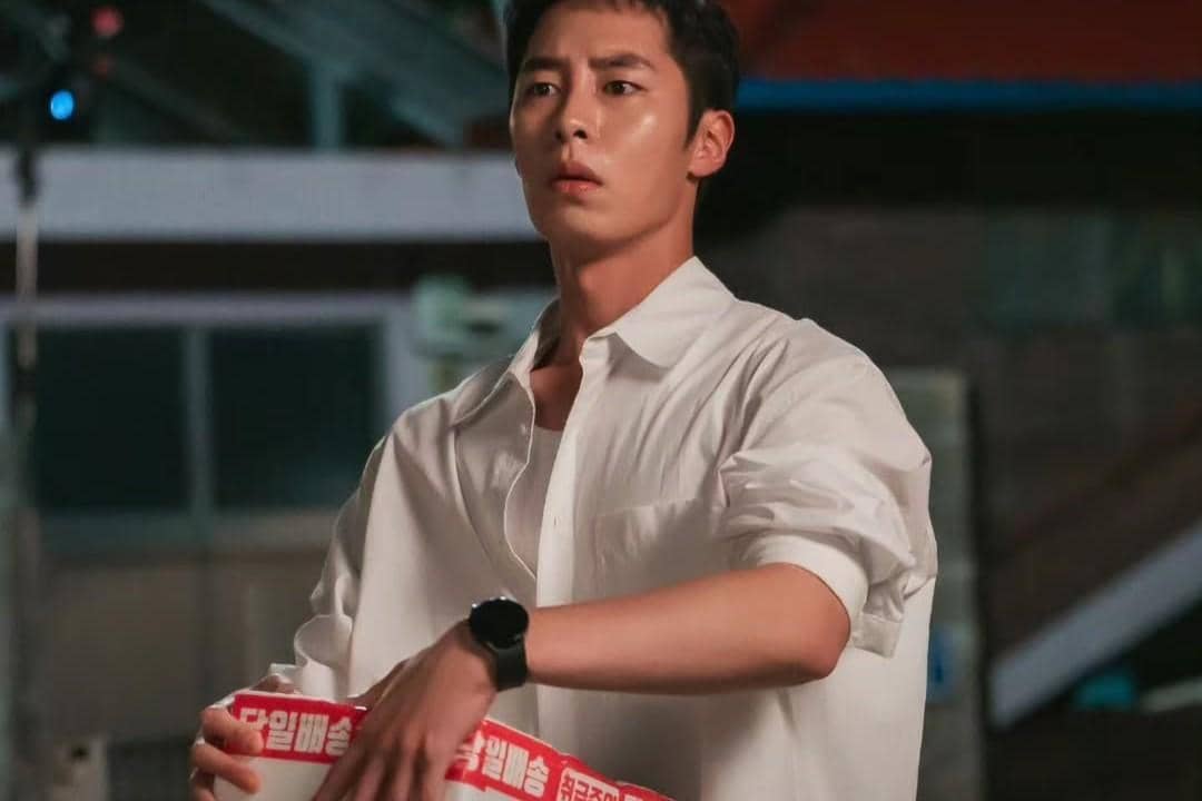 Seorang pria mengenakan kemeja putih memegang kotak berwarna merah dan putih dalam adegan drama Doctor On The Edge.