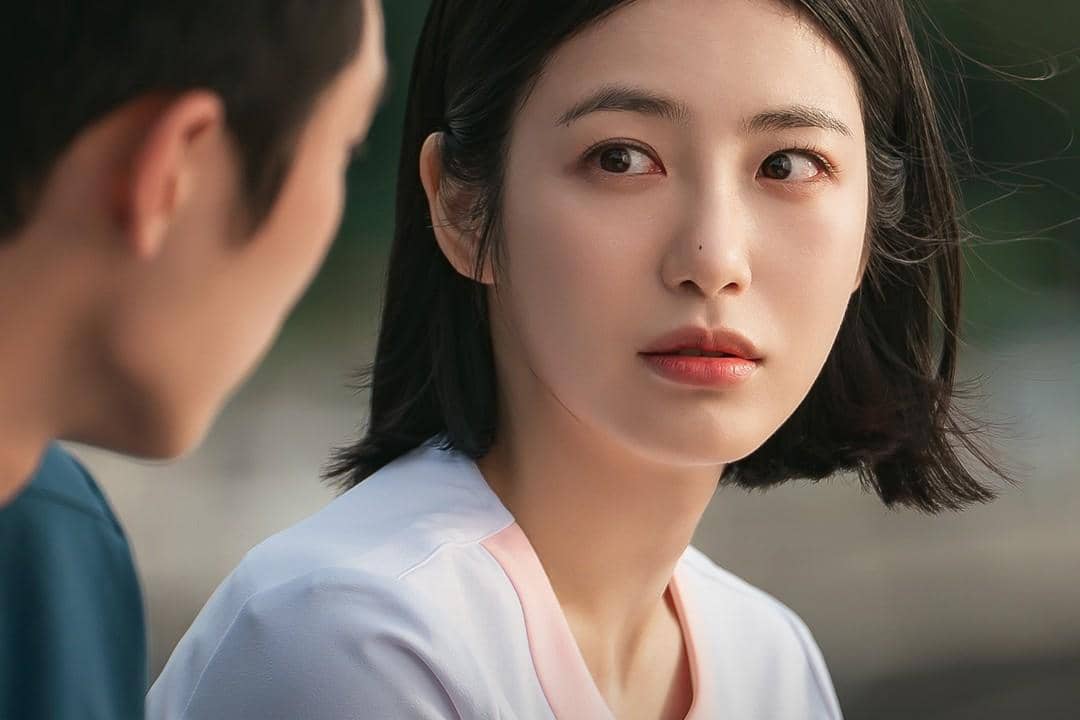 Seorang wanita berambut pendek mengenakan seragam medis berwarna putih muda menatap pria di depannya dalam adegan drama Doctor On The Edge.