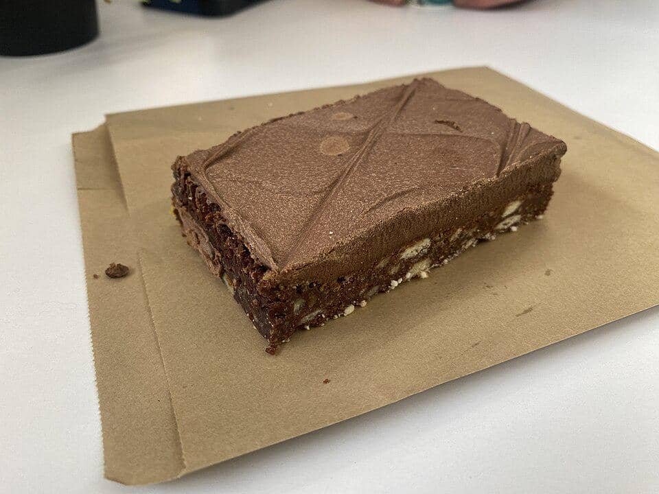 Potongan kue kalter hund berbentuk persegi panjang dengan lapisan cokelat tebal di atasnya, diletakkan di atas kertas cokelat.