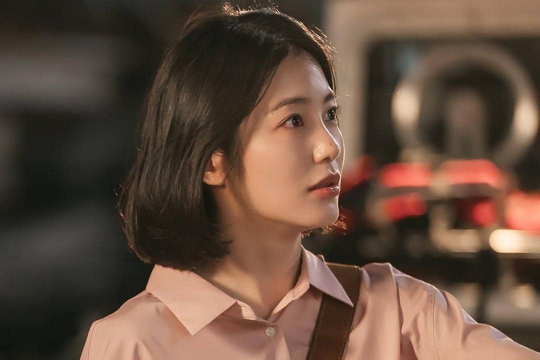 Seorang wanita berambut pendek mengenakan kemeja merah muda terlihat menatap ke samping dalam adegan drama Doctor on the Edge.